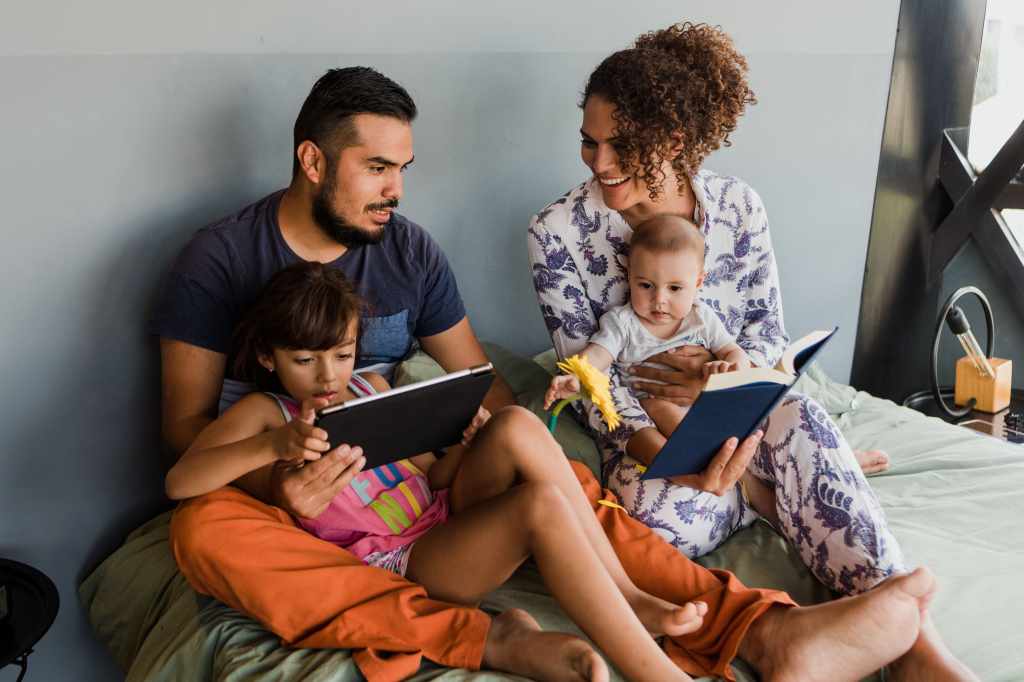 Family with two small children using their laptop in bed