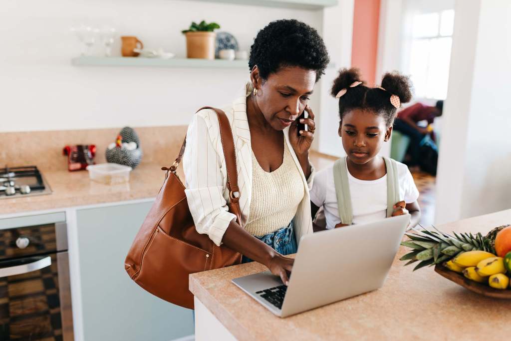 Photo of a woman talking on a mobile phone looking at her laptop on a kitchen counter