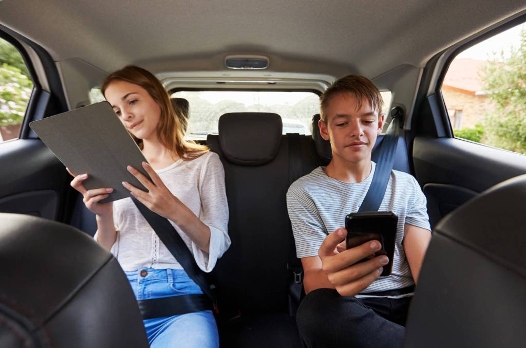 Photo f to teens in the back of a car looking at their mobile devices.